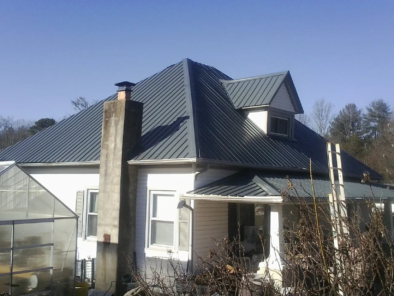 Dark blue standing seam metal roof on a white farmhouse with dormer — Slate & Tile Roof Repair by Roofing Brothers in Friesland