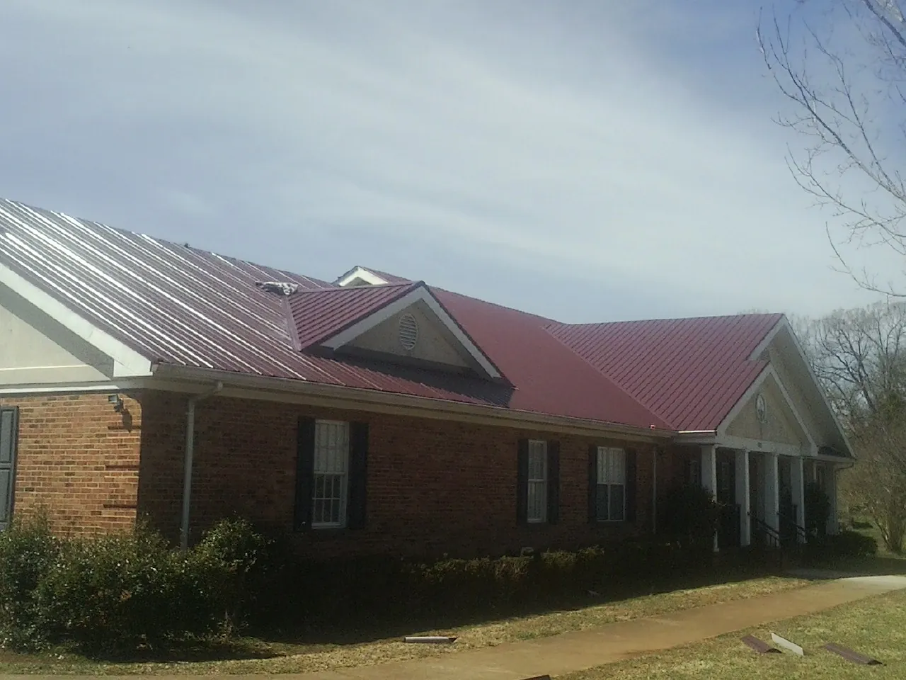 Red metal roof with gabled entries on a long brick building, from a Hail Damage Roof Repair job in Friesland
