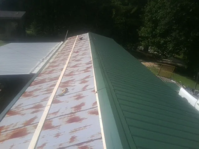 Old rusted panels beside newly installed green metal roofing — Wind Damage Roof Repair by Roofing Brothers in Friesland