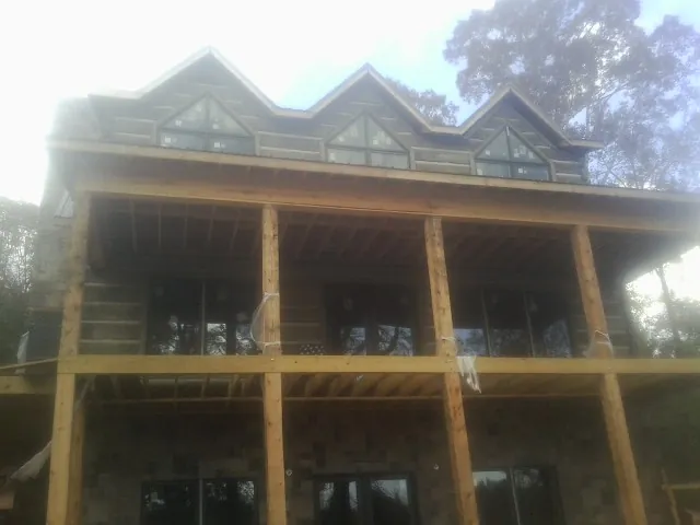 Dormers and porch framing on a large log home under construction — Roof Coating work by our crew in Friesland