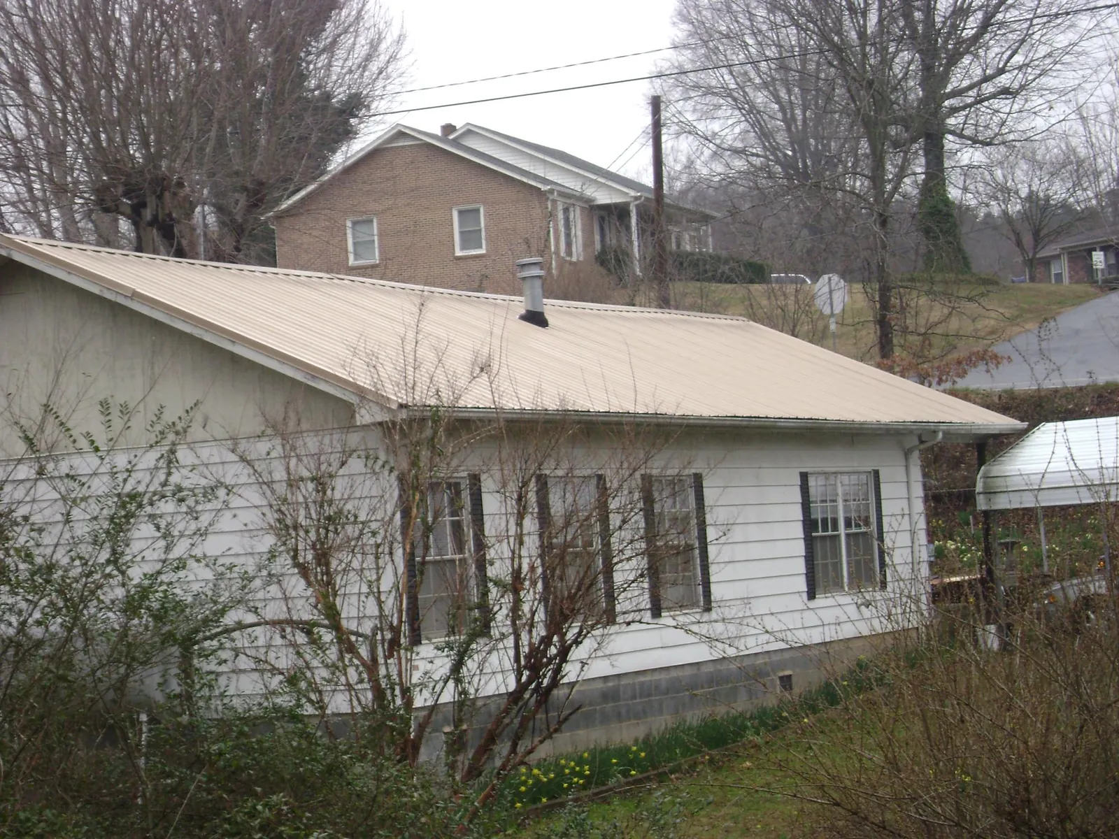 Tan metal roof on a white sided house set into a hillside — Commercial Roofing by Roofing Brothers in Friesland